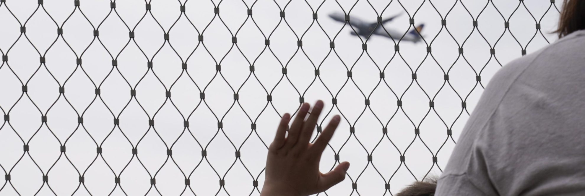 Symbolfoto Junge winkt hinter Absperrgitter dem Flugzeug hinterher