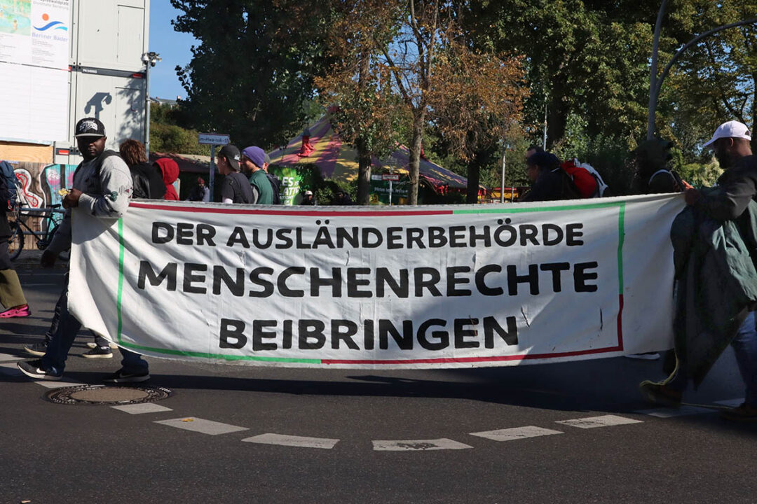 Menschen demonstrieren mit Banner: "Der Ausländerbehörde Menschenrechte beibringen"